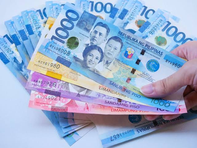 A hand holding a fan of Philippine peso banknotes.